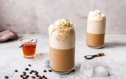 Eiskaffee selbst machen: Ein erfrischender Eiskaffee mit Sahne und Sirup, daneben Kaffeebohnen und Eiswürfel.