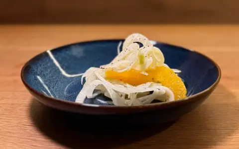 Ein erfrischender Fenchel-Orangen-Salat, garniert mit Pfeffer, in einer blauen Schale auf einem Holztisch.