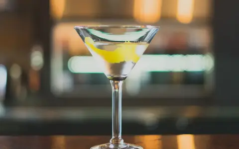 Ein klassischer Martini, perfekt für Ihr Martini Rezept. Mit Zitronenzeste garniert, steht er auf einer Holztheke.