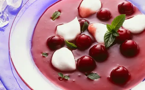 Erfrischende Kirschsuppe mit Sago, garniert mit Kirschen, Minze und weißen Tupfern.