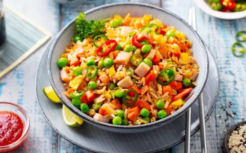 Schüssel mit Nasi Goreng: gebratener Reis mit Hühnchen, Erbsen, Karotten, Chili und Limettenspalten.