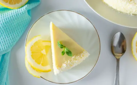 Ein Stück Philadelphia Torte Zitrone, garniert mit Minze und Kokosraspeln, neben Zitronenscheiben und einem Löffel.