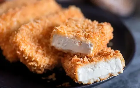Knusprig gebratenes Tofu auf einem Teller. Die goldbraune Panade umhüllt das weiche Innere. Perfekt, um Tofu knusprig braten zu lernen.