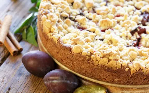 Ein saftiger Zwetschgenkuchen mit knusprigen Streuseln, daneben frische Zwetschgen und Zimtstangen. Perfekt für ein Streusel Rezept einfach!
