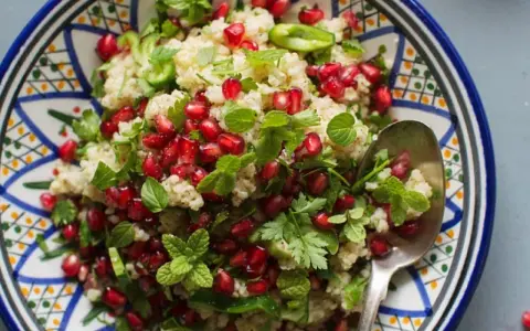 Bunter Couscous-Salat mit Granatapfelkernen, Minze und Petersilie in einer orientalisch gemusterten Schale.