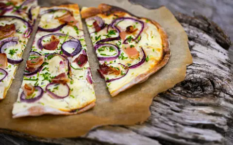 Flammkuchen mit klassischem Belag: Speck, Zwiebeln und Schnittlauch auf knusprigem Teig.