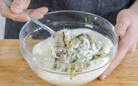 Matjes Hausfrauenart, Omas Rezept: Ein Löffel voll cremiger Sauce mit Matjesstücken und Dill wird aus einer Glasschüssel gehoben.
