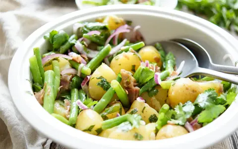 Frischer Kartoffel Bohnen Salat mit roten Zwiebeln und Kräutern in einer weißen Schüssel, bereit zum Servieren.