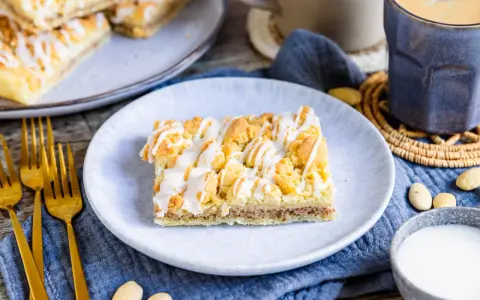 Ein Stück Prasselkuchen, wie aus einem DDR-Rezept, mit Zuckerguss und Streuseln. Dazu Kaffee und Mandeln.