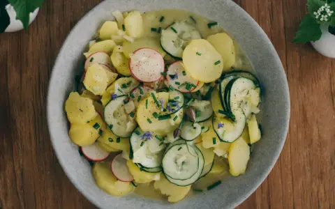 Ein Teller mit lauwarmer bayrischer Kartoffelsalat, garniert mit Radieschen, Gurken und Schnittlauch.