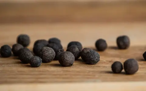 Eine Gruppe von Pimentkörnern liegt auf einem Holzbrett. Was ist Piment? Diese aromatischen Beeren duften nach Zimt, Nelken und Muskat.