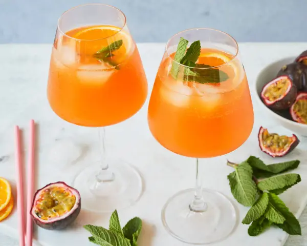 Zwei erfrischende Maracuja Spritz Cocktails mit Eis, Orangenscheiben und Minze, garniert mit frischen Passionsfrüchten.