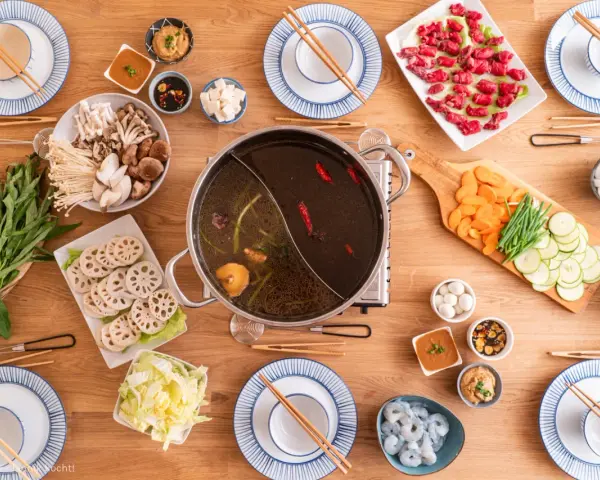 Zutaten für ein köstliches Hot Pot selber machen: Fleisch, Pilze, Gemüse, Garnelen und verschiedene Dips auf einem Holztisch arrangiert.