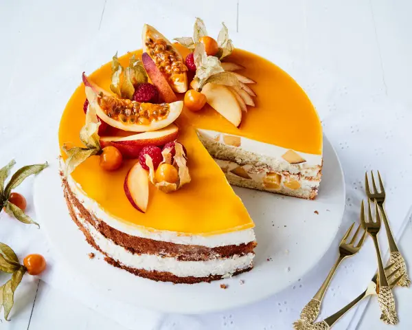 Eine köstliche Pfirsich Maracuja Torte mit frischen Früchten und Sahne. Ein Stück ist bereits angeschnitten.