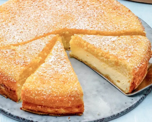 Ein saftiger Käsekuchen, bestäubt mit Puderzucker. Ein Stück wird gerade mit einem Tortenheber herausgehoben. Dreh dich um, Kuchen, du siehst köstlich aus!