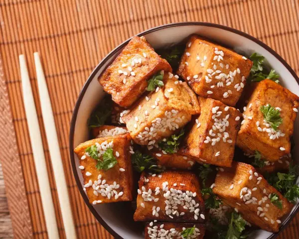 Knusprig gebratene Tofuwürfel mit Sesam und Petersilie in einer Schüssel. So schmeckt Tofu köstlich!