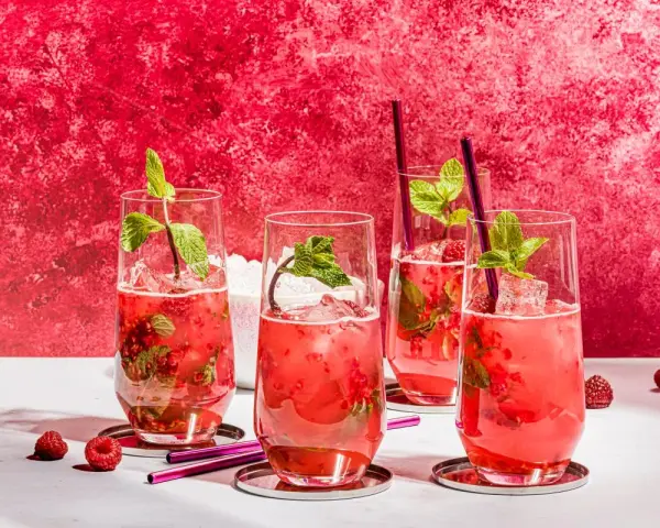 Vier erfrischende Bacardi Razz Mojitos mit Himbeeren und Minze, bereit zum Genießen.