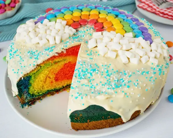Bunter, sommerlicher Kuchen mit Regenbogen-Schichten, weißen Marshmallows und bunten Smarties.