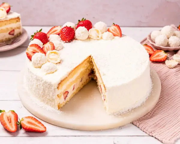Eine köstliche Erdbeer Raffaello Torte, verziert mit frischen Erdbeeren und Raffaello Kugeln, auf einem Marmorsockel.