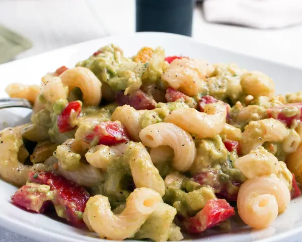 Cremiger nudelsalat mit avocado, Tomaten und Gewürzen auf einem weißen Teller.