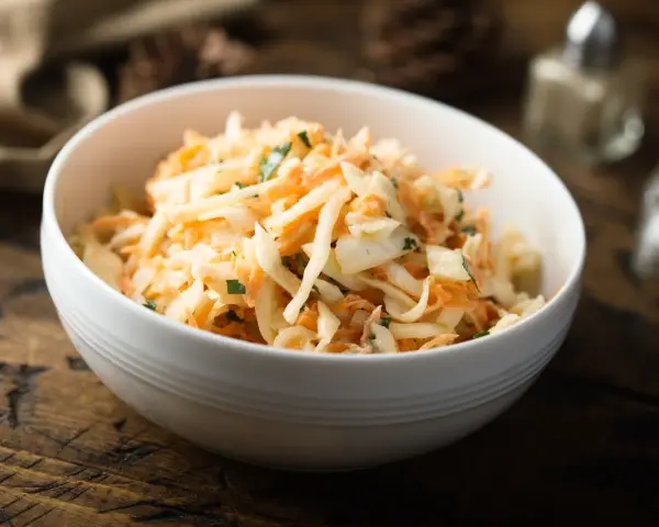 Schüssel mit cremigem Rettichsalat mit Apfel und Kräutern, serviert auf einem rustikalen Holztisch.