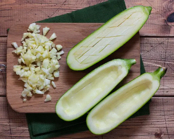 Vorbereitung für gefüllte Zucchini: ausgehöhlte Zucchinihälften und gehackter Knoblauch liegen bereit. Die Zucchini kerne essbar, werden oft mitverwendet.