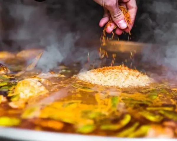 Gewürze werden über Reis und Gemüse gestreut, was zeigt, was ist paella: ein köstliches spanisches Reisgericht, das in einer großen Pfanne gekocht wird.