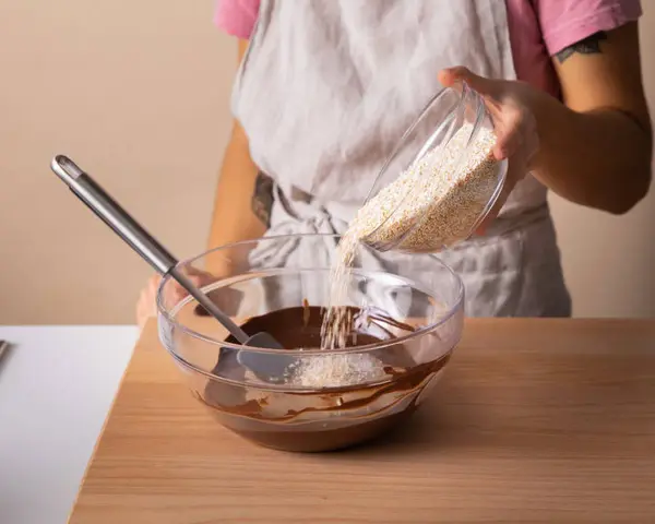 Eine Person gibt Amaranth zu geschmolzener Schokolade in einer Schüssel. Was ist Amaranth? Ein gesundes Getreide für leckere Rezepte.