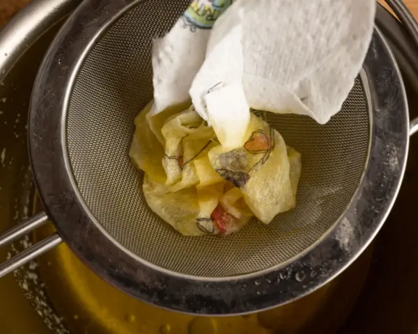 Ein Sieb hält ein Stück Papier mit Blumenmuster, das über einem Topf mit geschmolzener Butter liegt. Perfekt für raffinierte Butter Rezepte.