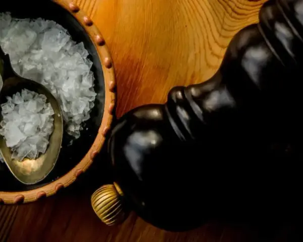Fleur de sel, zarten Salzkristallen auf einem Löffel in einer Schale, neben einer dunklen Pfeffermühle.
