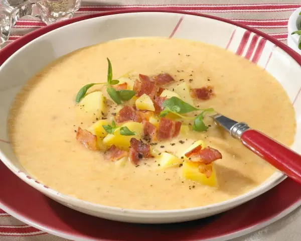 Eine dampfende, cremige Kartoffelsuppe mit Sahne, garniert mit Kartoffelwürfeln, knusprigem Speck und frischen Kräutern.