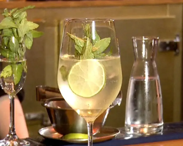 Erfrischender Hugo mit Limette und Minze, perfekt für ein Hugo Rezept. Daneben ein Glas mit Minze und eine Karaffe Wasser.