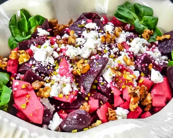 Rote Bete Salat mit Apfel, Feta und Walnüssen, garniert mit grünen Blättern. Ein farbenfroher und gesunder Genuss.