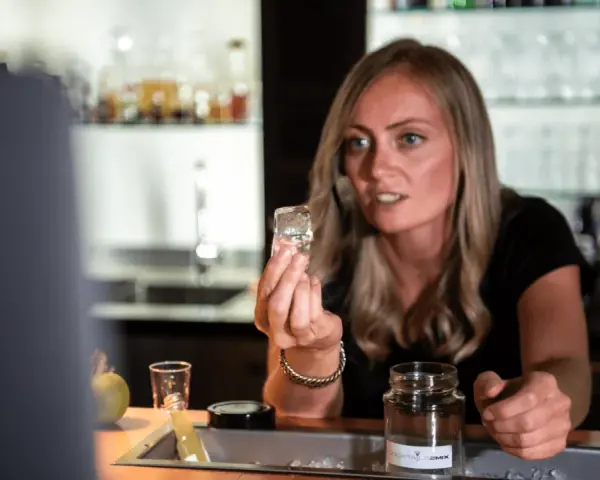 Eine Barkeeperin zeigt einen Eiswürfel, der für perfekte cocktail rezepte unerlässlich ist.