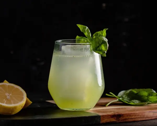 Erfrischender Basil Smash mit Zitrone und Basilikum garniert, serviert auf einem Holzbrett.