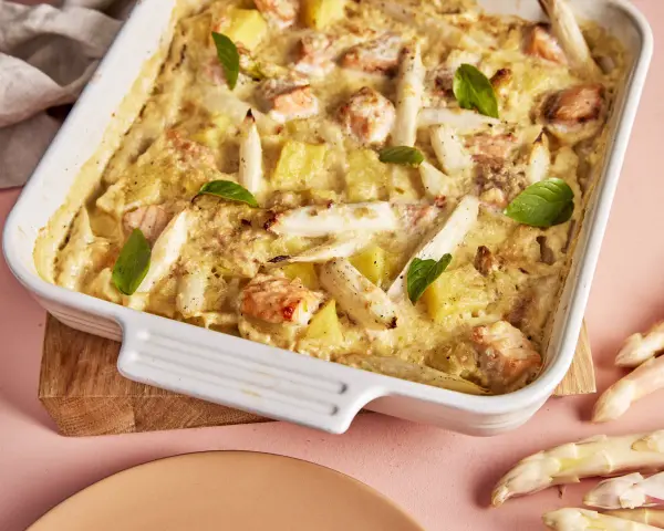 Ein köstlicher Spargel Lachs Auflauf in einer weißen Auflaufform, garniert mit Basilikum. Dazu frischer Spargel.