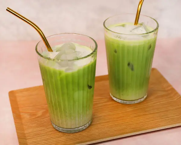 Zwei erfrischende Iced Matcha Latte mit goldenen Strohhalmen auf einem Holztablett. Perfekt für ein schnelles iced matcha latte rezept.