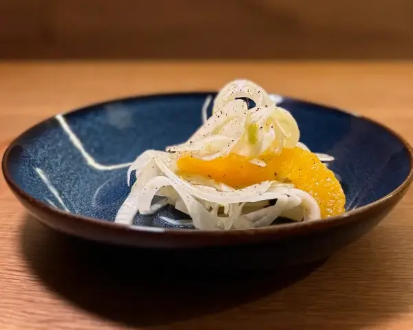 Ein erfrischender Fenchel-Orangen-Salat, garniert mit Pfeffer, in einer blauen Schale auf einem Holztisch.