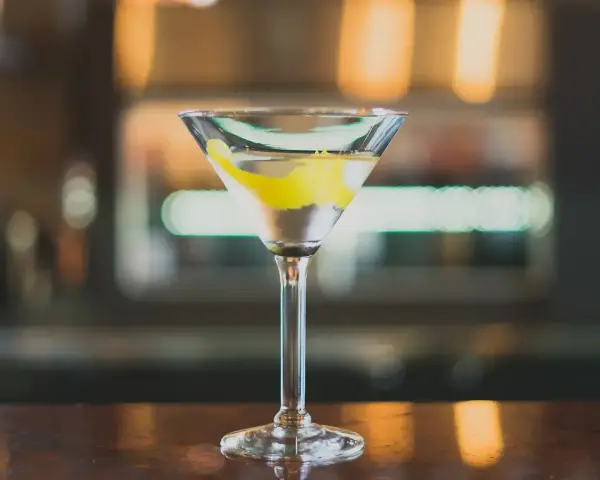 Ein klassischer Martini, perfekt für Ihr Martini Rezept. Mit Zitronenzeste garniert, steht er auf einer Holztheke.