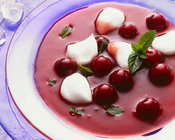 Erfrischende Kirschsuppe mit Sago, garniert mit Kirschen, Minze und weißen Tupfern.