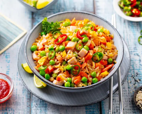 Schüssel mit Nasi Goreng: gebratener Reis mit Hühnchen, Erbsen, Karotten, Chili und Limettenspalten.
