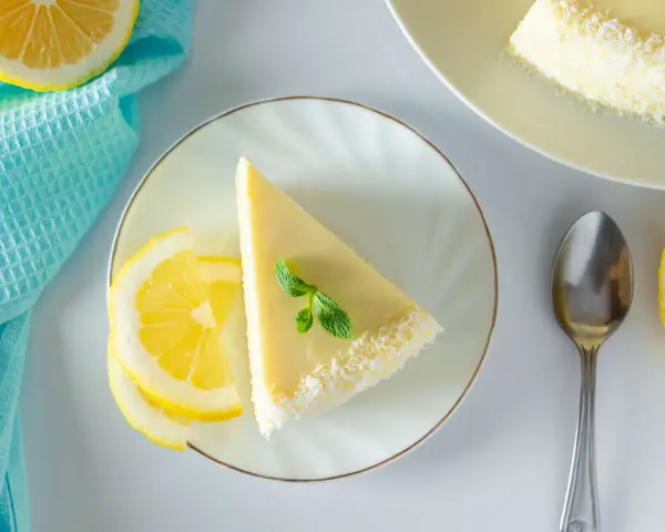 Ein Stück Philadelphia Torte Zitrone, garniert mit Minze und Kokosraspeln, neben Zitronenscheiben und einem Löffel.