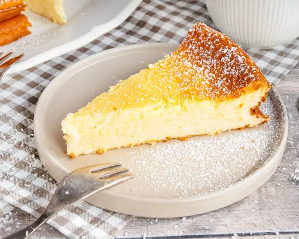 Ein saftiges Stück Kokoskuchen mit Pudding, gebacken in einer Springform, bestäubt mit Puderzucker.