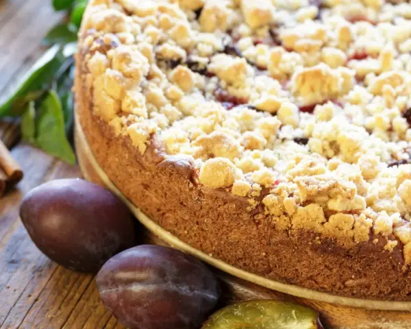 Ein saftiger Zwetschgenkuchen mit knusprigen Streuseln, daneben frische Zwetschgen und Zimtstangen. Perfekt für ein Streusel Rezept einfach!