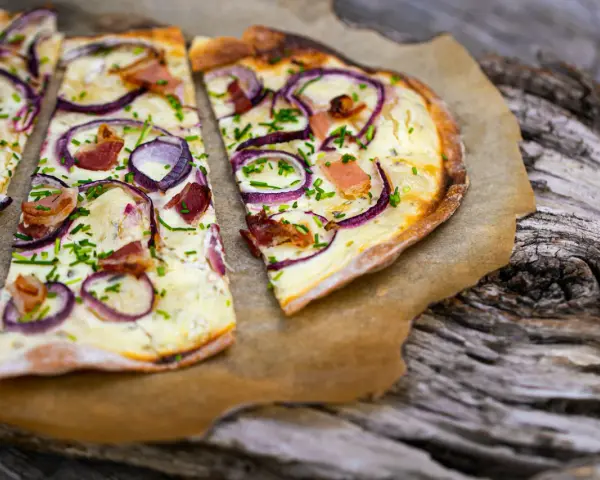 Flammkuchen mit klassischem Belag: Speck, Zwiebeln und Schnittlauch auf knusprigem Teig.