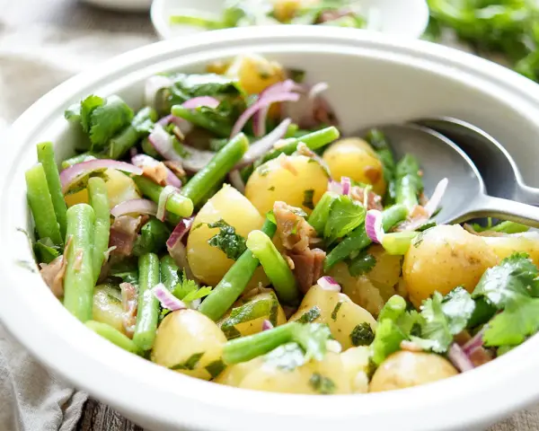 Frischer Kartoffel Bohnen Salat mit roten Zwiebeln und Kräutern in einer weißen Schüssel, bereit zum Servieren.