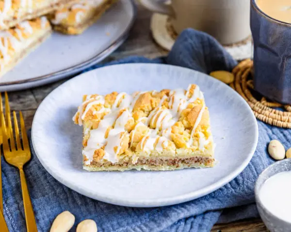 Ein Stück Prasselkuchen, wie aus einem DDR-Rezept, mit Zuckerguss und Streuseln. Dazu Kaffee und Mandeln.