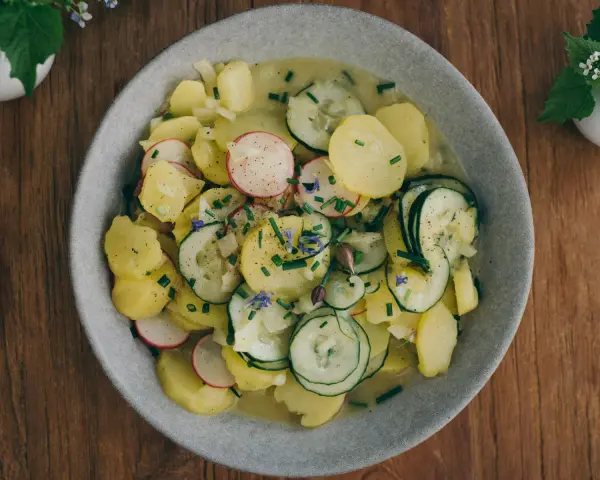Ein Teller mit lauwarmer bayrischer Kartoffelsalat, garniert mit Radieschen, Gurken und Schnittlauch.