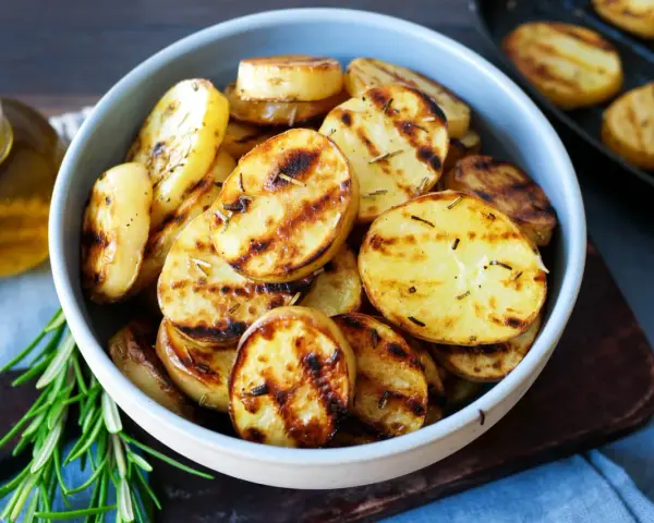 Schmackhafte Kartoffelscheiben mit Rosmarin, perfekt gegrillt. Die Streifen vom Grill sind deutlich sichtbar.