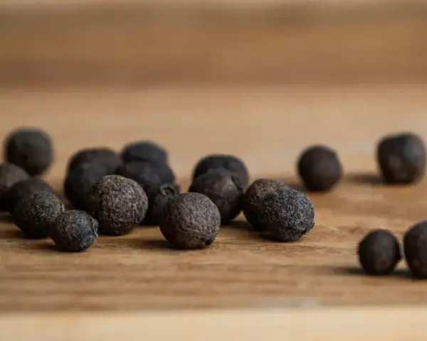 Eine Gruppe von Pimentkörnern liegt auf einem Holzbrett. Was ist Piment? Diese aromatischen Beeren duften nach Zimt, Nelken und Muskat.